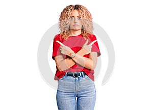 Young blonde woman with curly hair wearing casual red tshirt pointing to both sides with fingers, different direction disagree