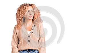 Young blonde woman with curly hair wearing casual winter jumper smiling looking to the side and staring away thinking