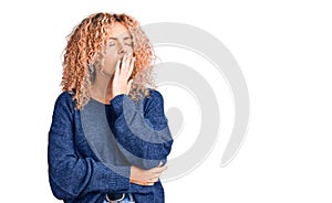 Young blonde woman with curly hair wearing casual winter sweater bored yawning tired covering mouth with hand