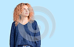 Young blonde woman with curly hair wearing casual winter sweater smiling looking to the side and staring away thinking