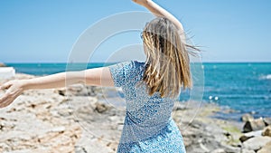 Young blonde woman dancing backwards at seaside