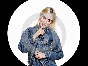 Young blonde woman in denim jaket and jeans shows Index finger to the lips on white background