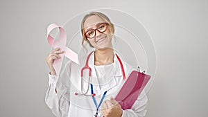 Young blonde woman doctor holding breast cancer awareness pink ribbon and clipboard over isolated white background