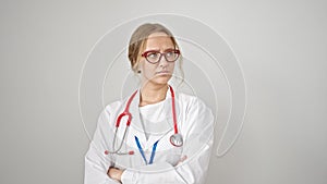 Young blonde woman doctor standing with serious expression and arms crossed gesture over isolated white background