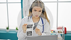 Young blonde woman doctor on video call showing baby ultrasound at clinic