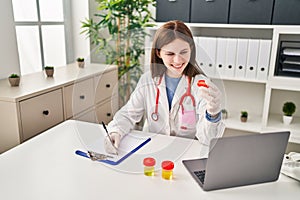 Young blonde woman doctor writing medical report holding empty test tube at clinic