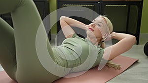 Young blonde woman doing abs exercise lying on floor at sport center