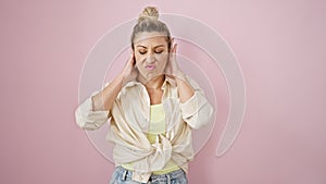 Young blonde woman doing derision expression with hands on ears over isolated pink background