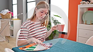 Young blonde woman drinking coffee choosing paint color at dinning room