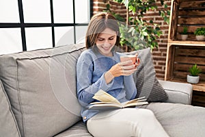 Young blonde woman drinking coffee reading book at home