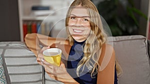 Young blonde woman drinking coffee sitting on sofa at home