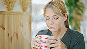 Young blonde woman drinking coffee sitting on table at coffee shop