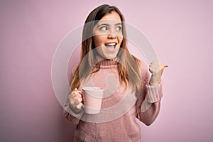Young blonde woman drinking a cup of coffee over pink isolated background pointing and showing with thumb up to the side with