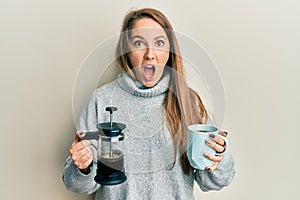 Young blonde woman drinking a cup of italian coffee afraid and shocked with surprise and amazed expression, fear and excited face