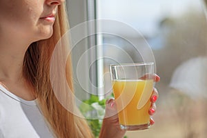 Young blonde woman drinking orange juice and looking at the window