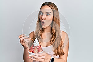 Young blonde woman eating strawberry ice cream afraid and shocked with surprise and amazed expression, fear and excited face