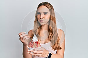 Young blonde woman eating strawberry ice cream puffing cheeks with funny face