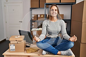 Young blonde woman ecommerce business worker doing yoga sitting on table at office