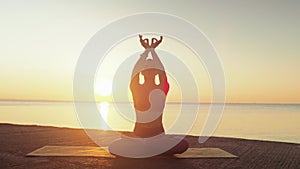 Young blonde woman engaged in yoga on the beach by the sea background of the sunrise or sunset