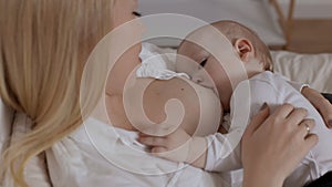 Young blonde woman feeding with breast and stroking her baby boy. Concept of breastfeeding, maternity and child