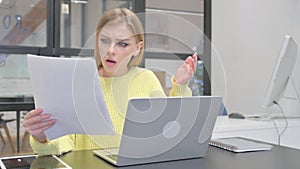 Young Blonde Woman Feeling Shocked while Working on Documents and Laptop