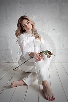 A young blonde woman with a flower in her hands is sitting on the floor