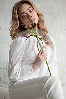 A young blonde woman with a flower in her hands is sitting on the floor