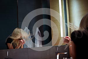 Young blonde woman in front of mirror in the restroom with disco mirror ball