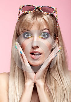 Young blonde woman with fun candy glasses on pink background