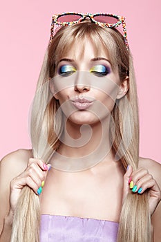 Young blonde woman with fun candy glasses on pink background