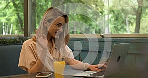 Young Blonde Woman with Glasses Using Laptop for Video Call While Sitting in Cafe, Fresh Orange Juice on Table