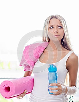 Young blonde woman going fitness sport with towel, bottle of water and yoga mat