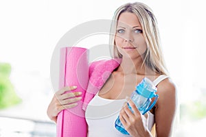 Young blonde woman going fitness sport with towel, bottle of water and yoga mat