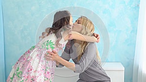 Young blonde woman and her teenage daughter hugging and kissing each other