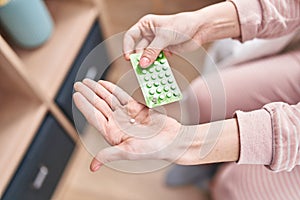 Young blonde woman holding birth control pills sitting on bed at bedroom