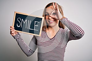 Young blonde woman holding blackboard with smile message over isolated white background with happy face smiling doing ok sign with