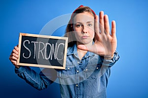 Young blonde woman holding blackboard with strong message over isolated blue background with open hand doing stop sign with