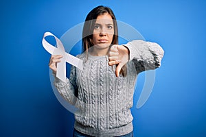 Young blonde woman holding cancer awareness and stop women violence white ribbon with angry face, negative sign showing dislike