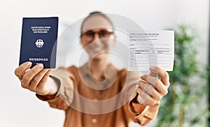 Young blonde woman holding covid vaccination record card and deutschland passport at waiting room