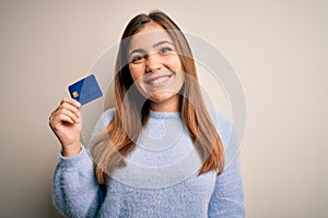 Young blonde woman holding credit card as payment over isolated background with a happy face standing and smiling with a confident