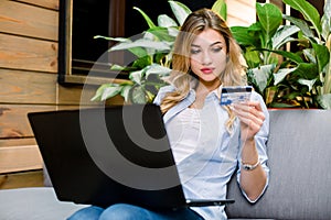 Young blonde woman holding credit card and using laptop computer. Online shopping concept, travelling, booking tickets