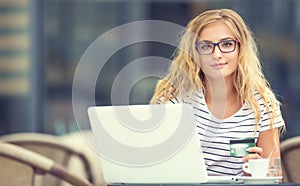 Young blonde woman holding credit card and using laptop computeron the terrace of the caf