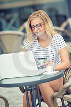 Young blonde woman holding credit card and using laptop computeron the terrace of the caf