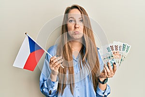 Young blonde woman holding czech republic flag and koruna banknotes depressed and worry for distress, crying angry and afraid