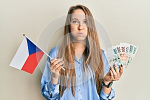 Young blonde woman holding czech republic flag and koruna banknotes puffing cheeks with funny face