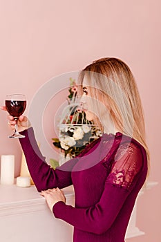 A young blonde woman holding a glass of red wine indoors