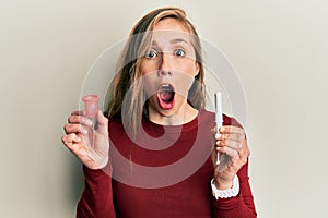 Young blonde woman holding menstrual cup and tampon afraid and shocked with surprise and amazed expression, fear and excited face