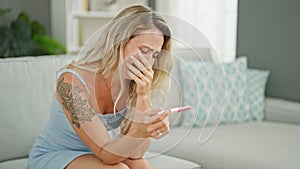 Young blonde woman holding pregnancy test crying at home