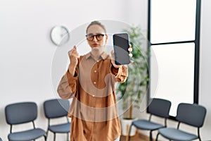 Young blonde woman holding smartphone showing blank screen annoyed and frustrated shouting with anger, yelling crazy with anger