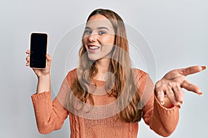 Young blonde woman holding smartphone showing screen celebrating achievement with happy smile and winner expression with raised